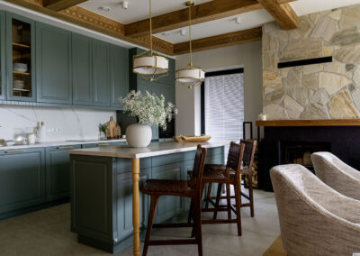 Kuchnia z wyspą i wysokimi krzesłami z ciemnego drewna, w tle kominek.