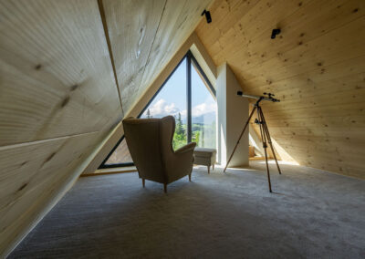 pokój na poddaszu z wygodnym krzesłem skierowanym w kierunku okna z widokiem na góry, luneta do oglądania gwiazd