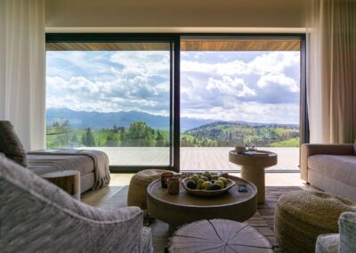 Widok z salony. Po środku znajduje się okrągły, drewniany stół. W tle wyjście na taras z widokiem