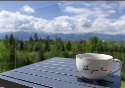 Filiżanka na stole, w tle zielone drzewa i niebieskie niebo z ciężkimi chmurami