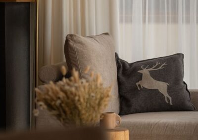Detal salonu z kanapą w jasnych kolorach lampą stojącą i poduszką z motywem jelenia