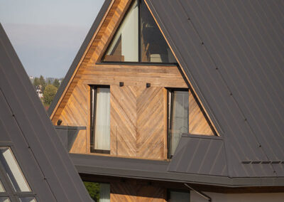 zbliżenie na dwa domy w stylu zakopiańskim ze skośnym szray dachem i ścianą obłożoną drewnem